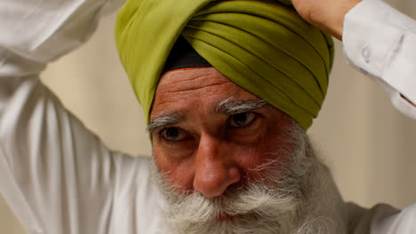 Primer-Plano-De-Un-Estudio-De-Un-Hombre-Sikh-Mayor-Con-Barba-Que-Usa-Una-Aguja-De-Salai-Al-Ponerse-Un-Turbante-Contra-Un-Fondo-Liso-4